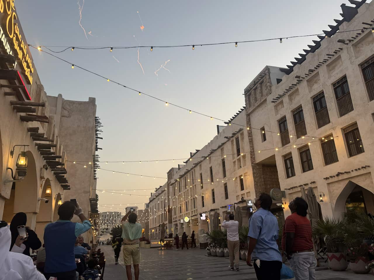 People in a street look up at missiles being intercepted in the evening sky.