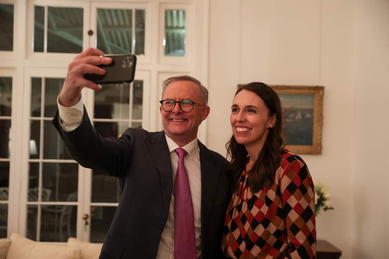 Anthony Albanese stands next to Jacinda Ardern and takes a selfie using his phone.