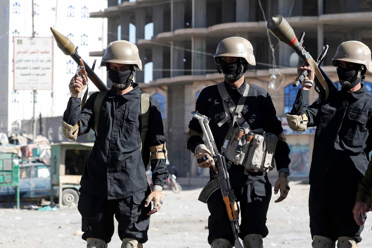 People wearing dark clothing, hard hats, and masks who are carrying weapons.