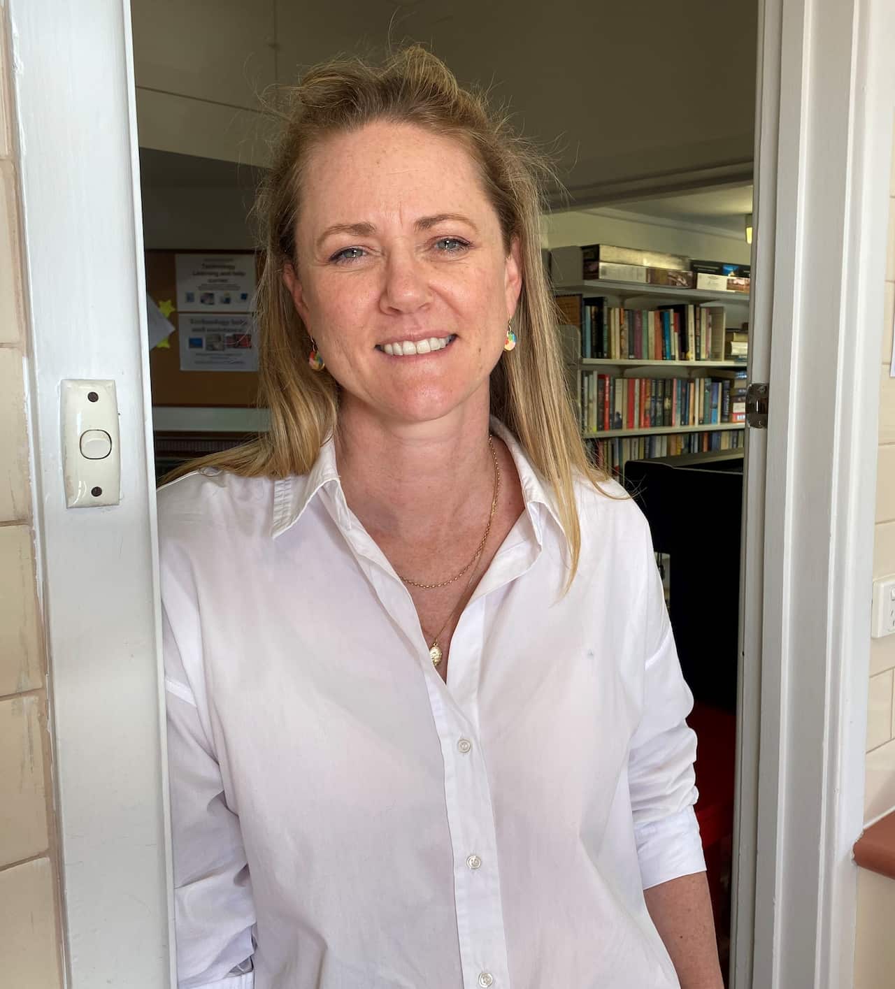 A woman with blonde hair standing in a white shirt.