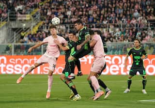 Football players wearing pink, black and green jerseys jump towards a football flying through the year.