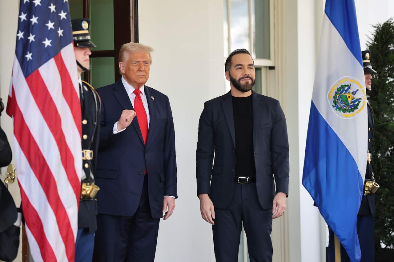 US president Donald Trump and El Salvador president Nayib Bukele stand side by side between two poles carrying the flags of both countries and two guards