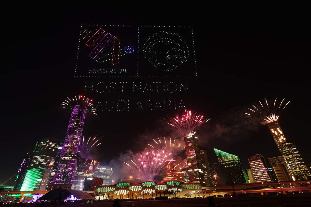 A drone show is seen displaying the words "Host Nation Saudi Arabia" above city skyline.