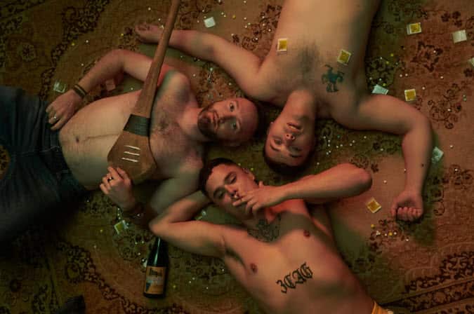 Aerial view of three topless men lying on the floor, surrounded by drugs