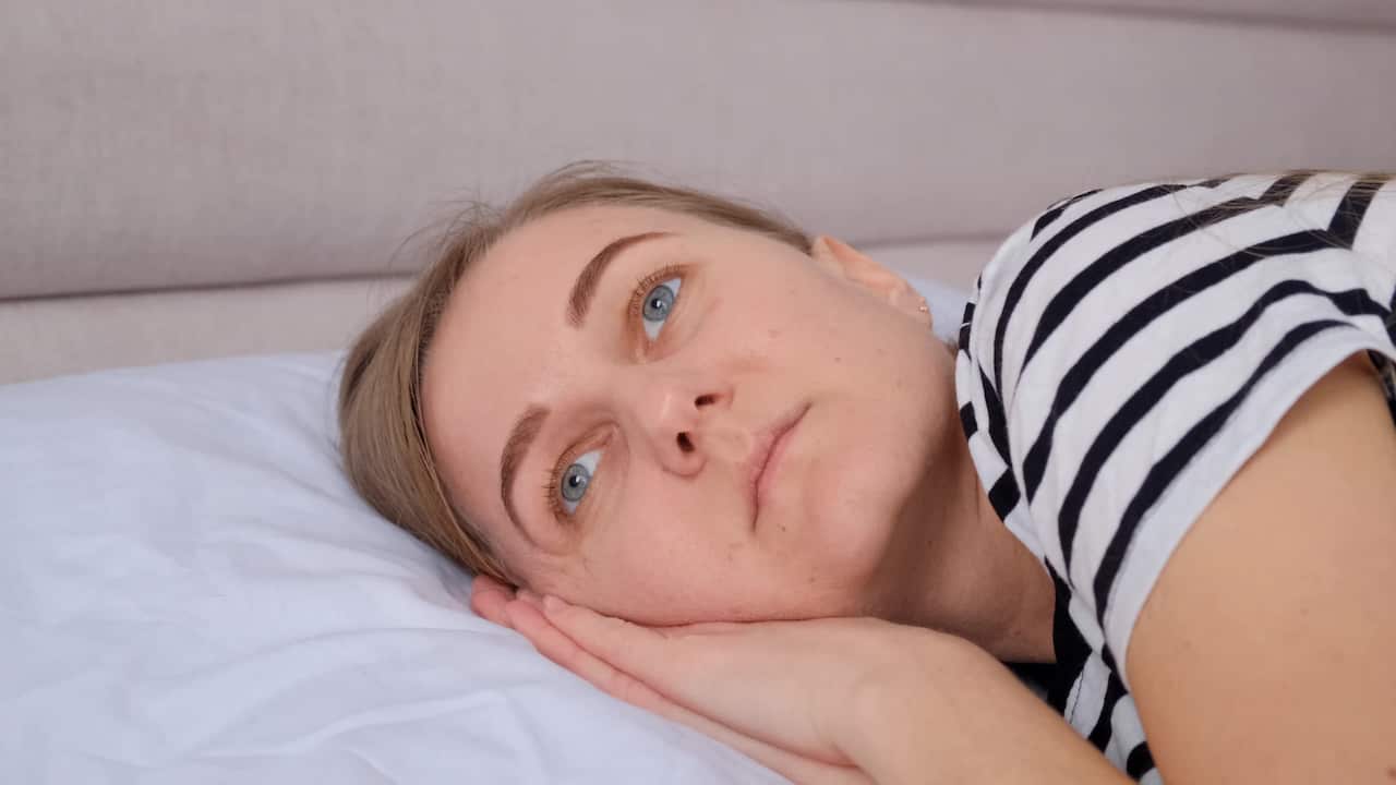 A woman wearing a striped top is lying sideways on a bed with her hands folded under her face.