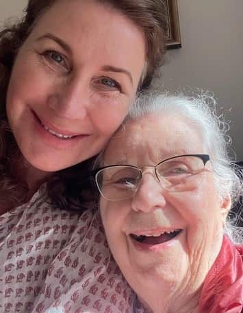 A woman and her mother with their heads next to each other smile for a selfie