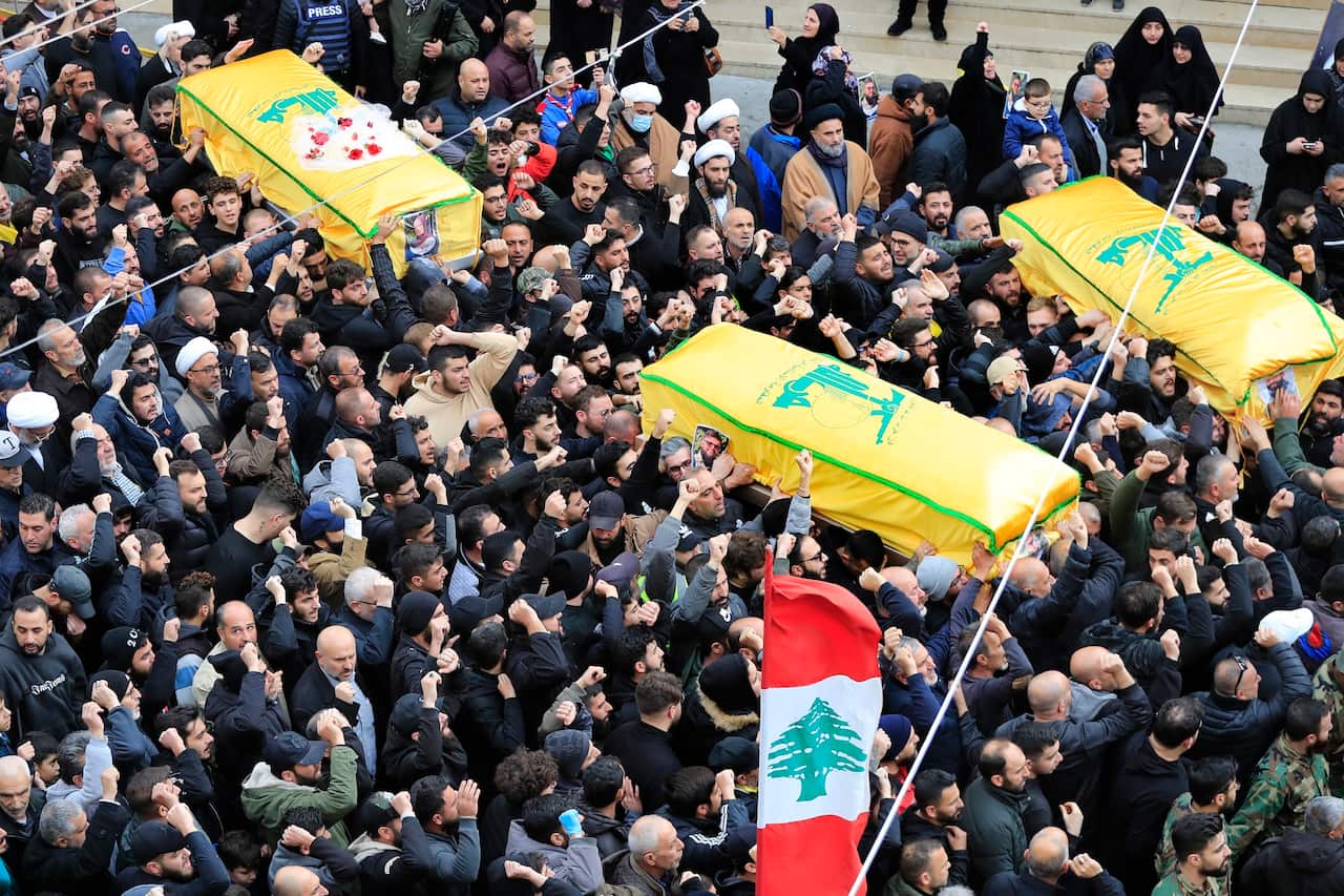 The funeral procession features the coffin being carried by individuals dressed in military uniforms.