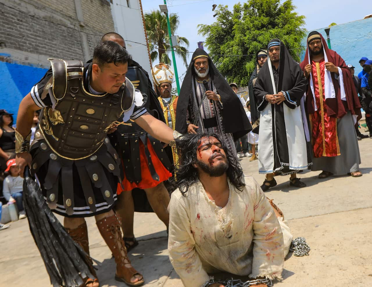 A man wearing a roman centurion's uniform holds up by the hair a man lying prostrate with tattered robes and a bleeding face.