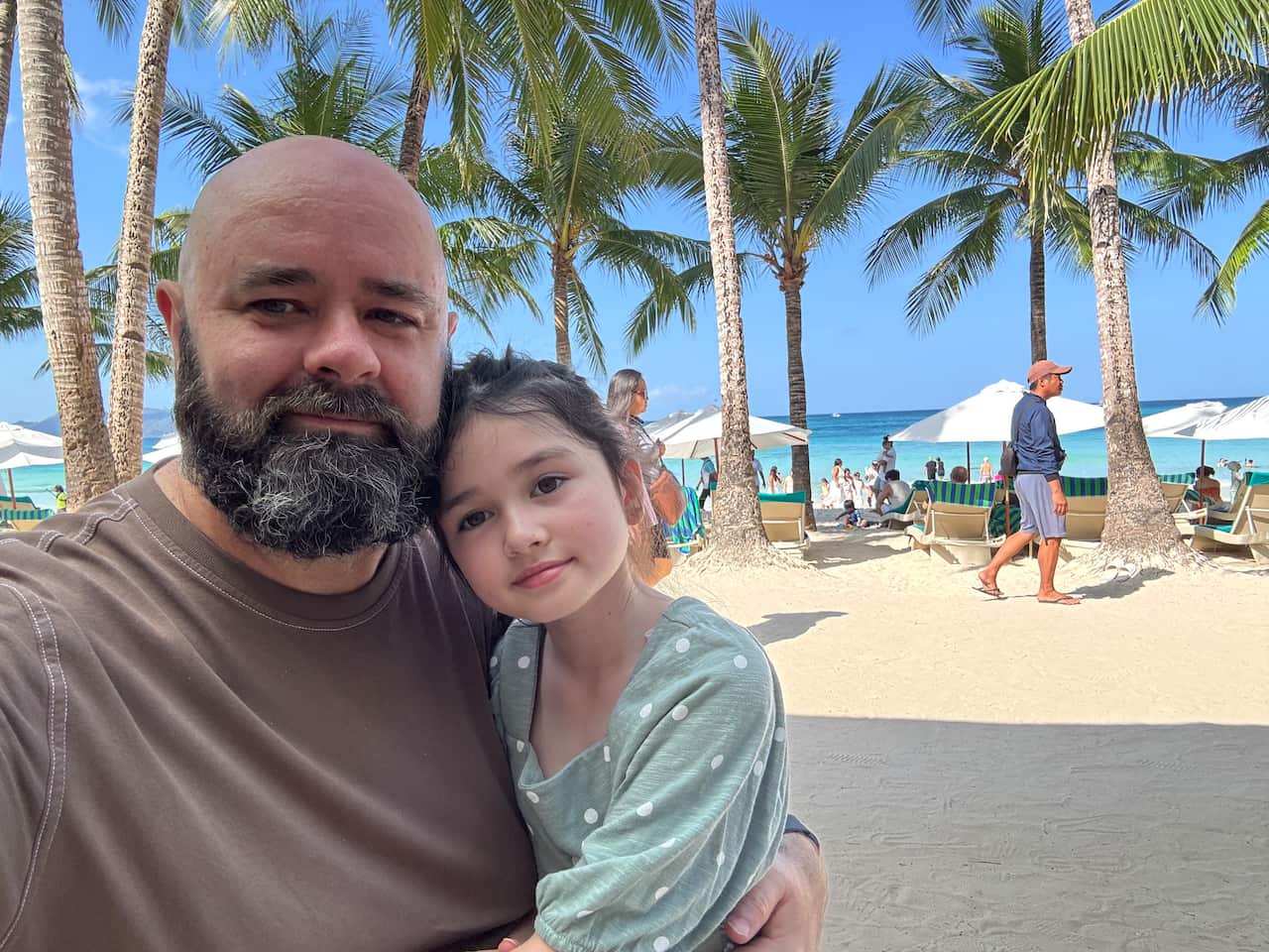A man and a child posing for a selfie on a beach.
