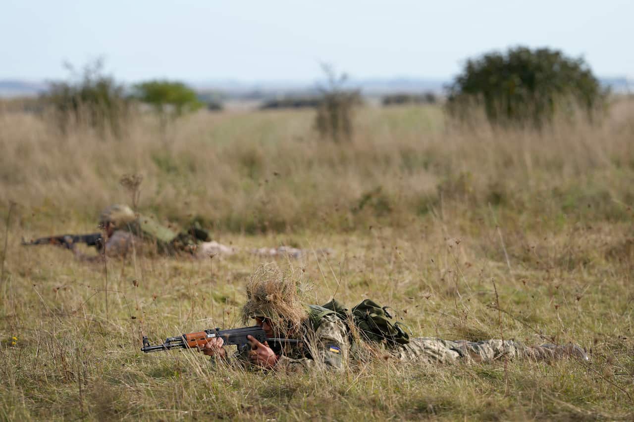 Soldiers wearing camouflage gear on the ground holding guns.