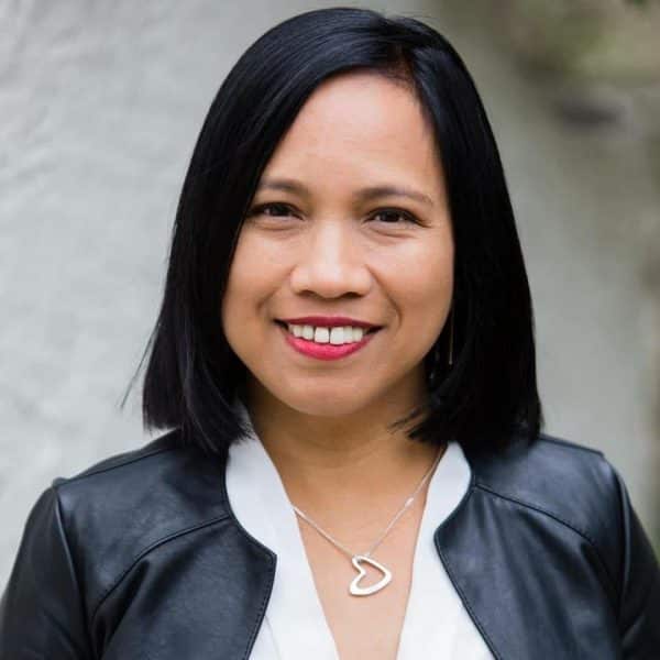 A woman in a black jacket and white shirt is smiling.