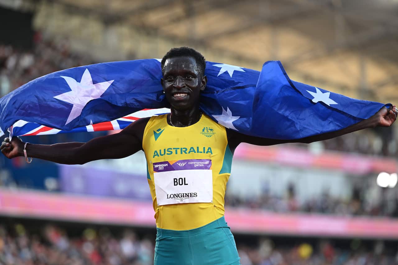 A man wearing a green and yellow outfit runs with an Australian flag over his shoulders 