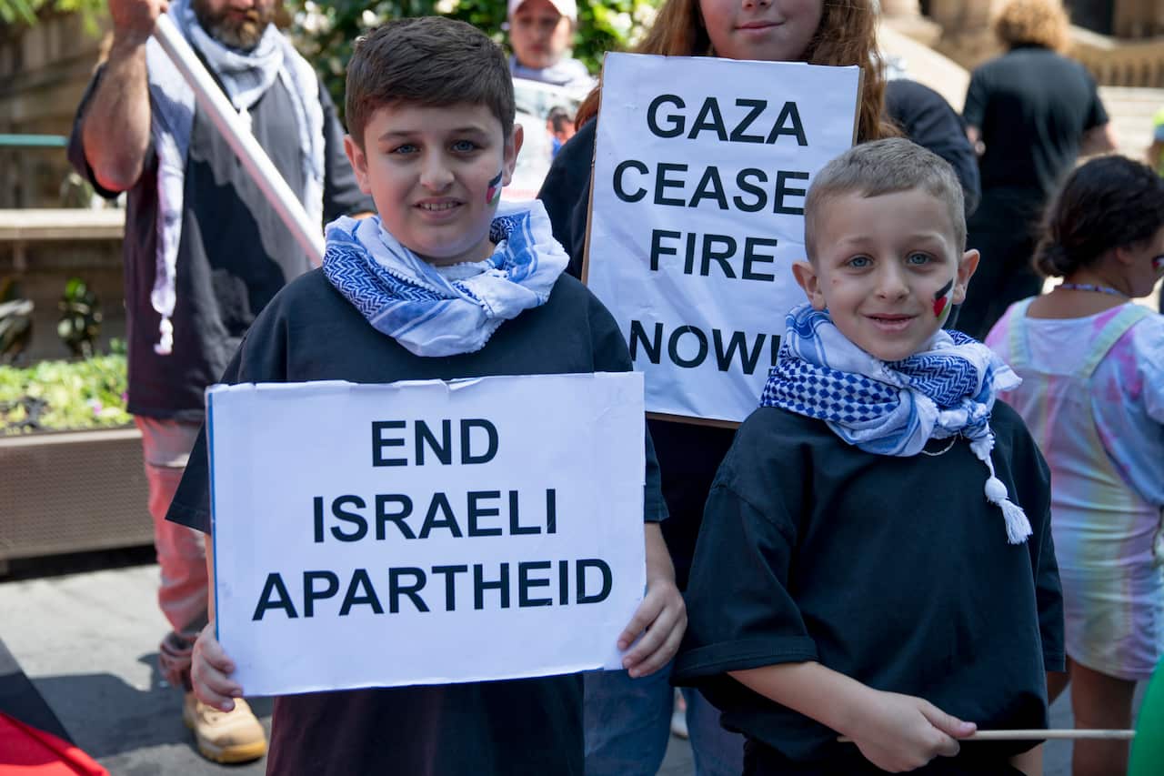 Two young boys wearing keffiyah and carrying signs reading "End Israeli Apartheid".