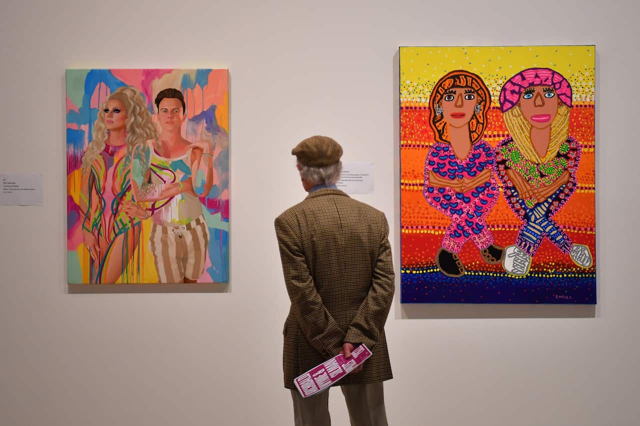A man looks at two colourful paintings on a wall in an art gallery