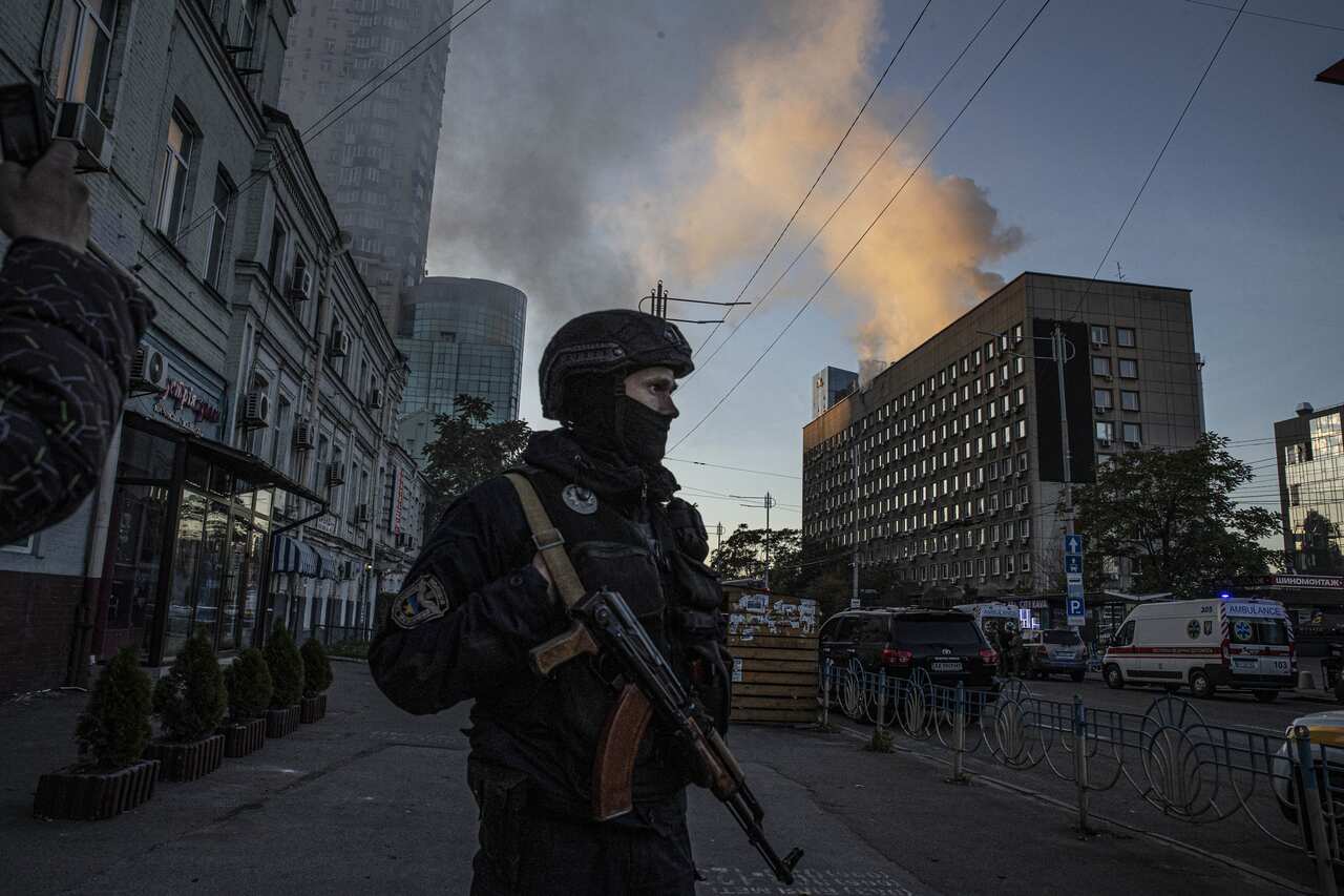 A Ukrainian soldier standing on a street. Smoke appears to be coming from a building behind them.