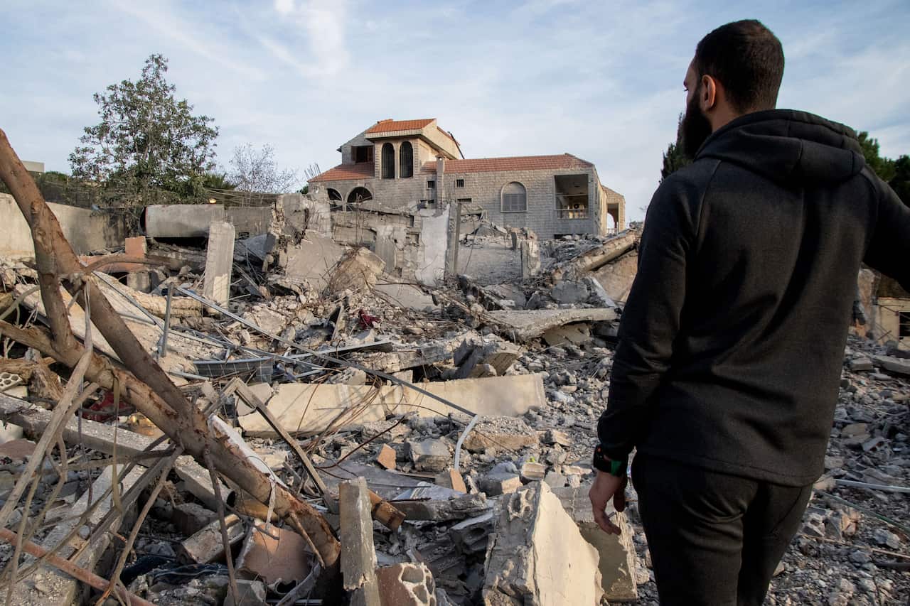 A man stands in front of homes destroyed during the conflict