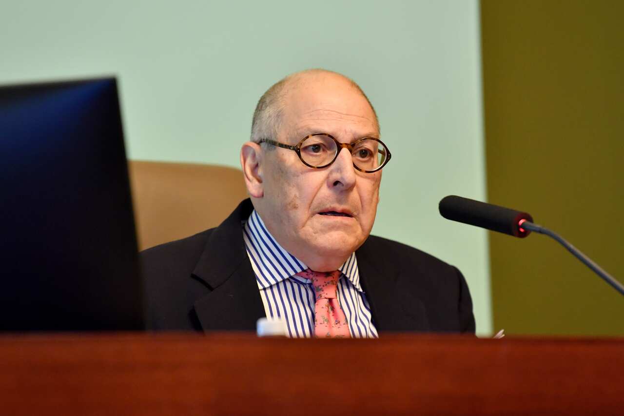 A man speaking into a microphone on a bench.