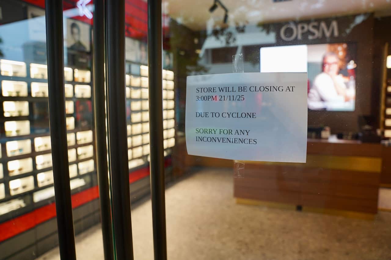 An OPSM optometry retailer with an A4 paper sign stuck to the glass front door informing the public it will be closed due to a cyclone.