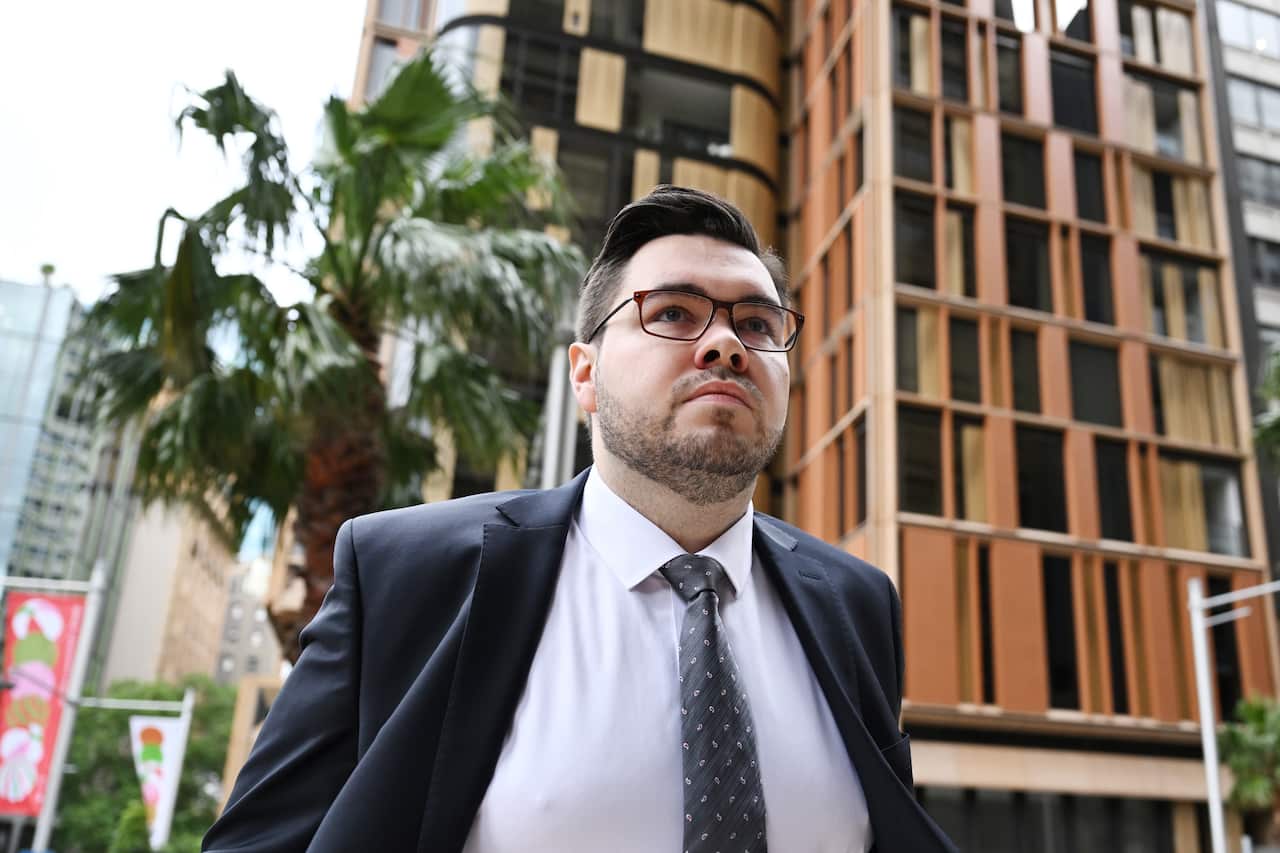A man in a black suit, white shirt and blue and white tie