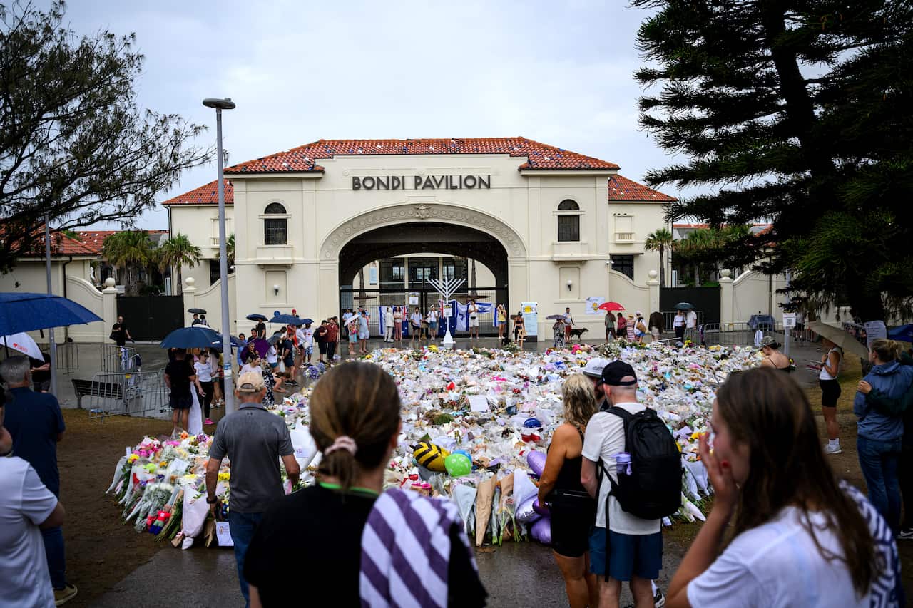 Flowers and other tributes on the ground outside Bondi Pavilion, where people are gathered.