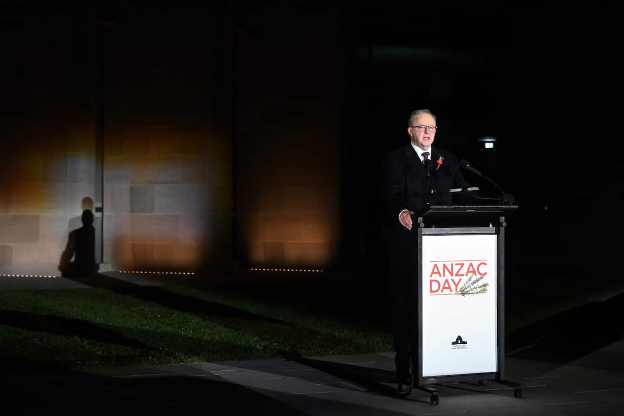 Anthony Albanese, in a black suit, speaks at a podium with the words Anzac Day written on its front.