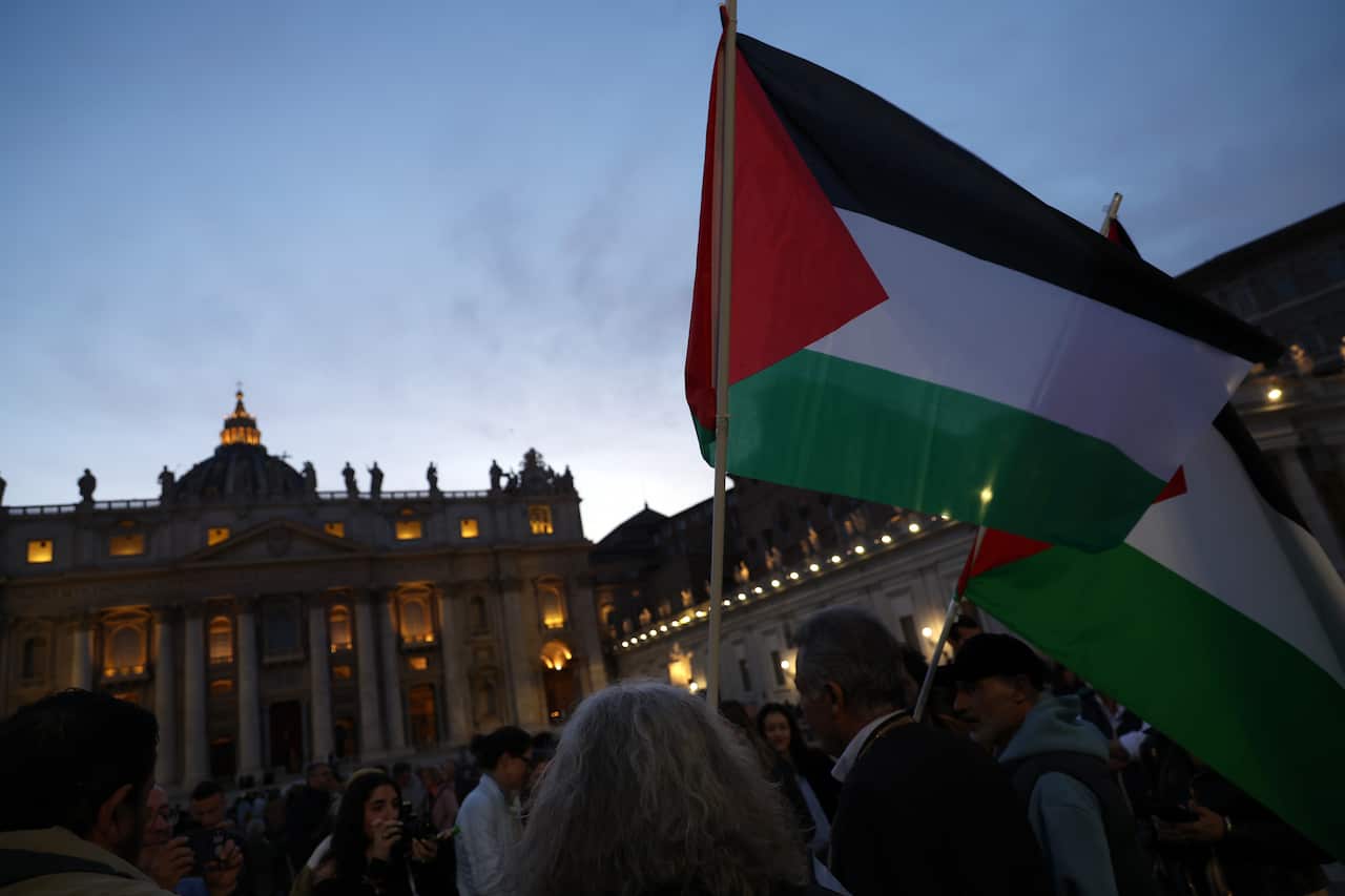 People raise Palestinian flags outside a building at nightfall.