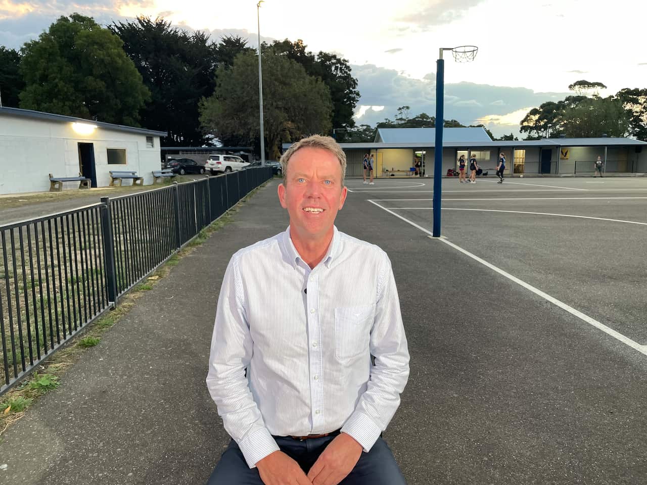 A man in a white shirt sits near a basketball court. 