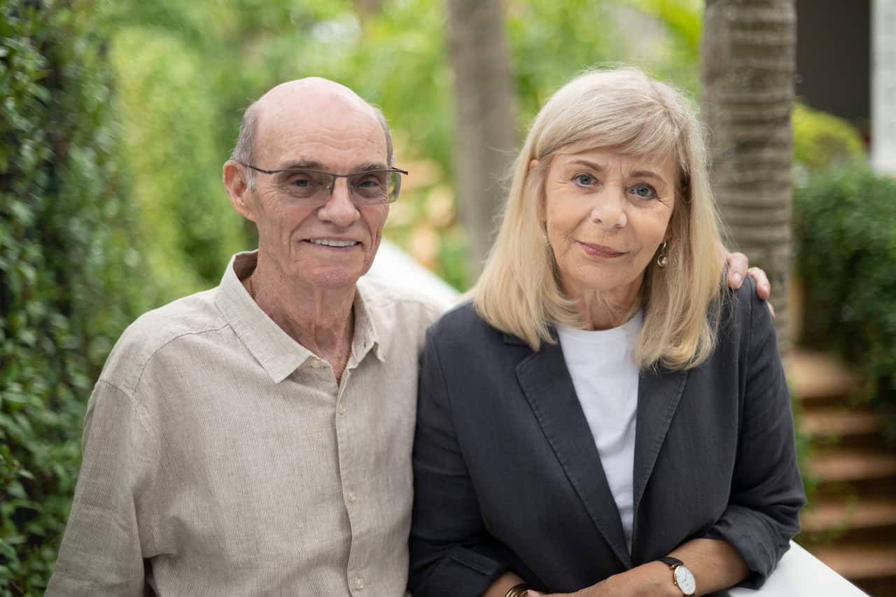 A middle-aged man (left) with his arm around a middle-aged woman. They are both looking at the camera, the man smiling.