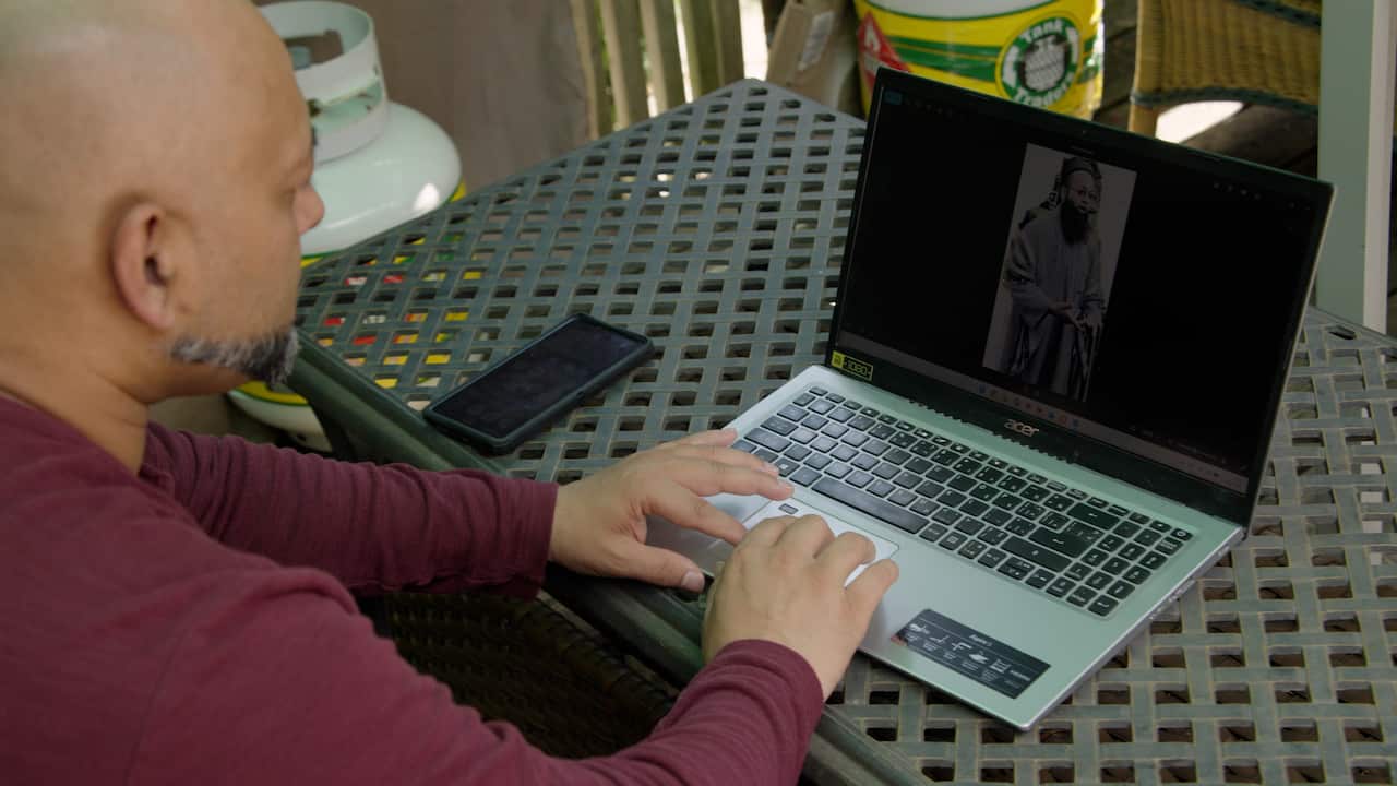 A man in a maroon jumper typing at a laptop