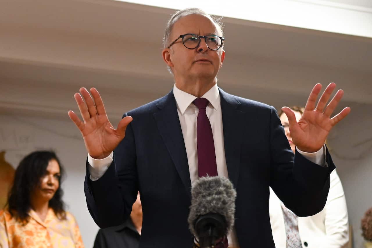 Man in a suit gestures broadly in front of a microphone.