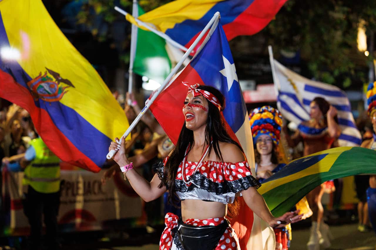 A woman taking part in a parade, waving a Chilean flag. She is wearing a red and white spotted scarf in  her hair, top, and skirt