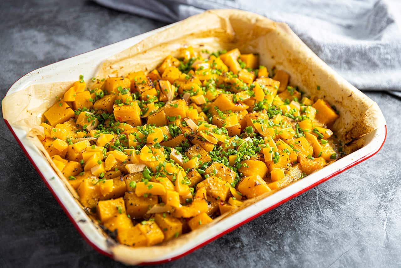 A baking dish holds cooked cubs of pumpkin, topped with chopped chives. 