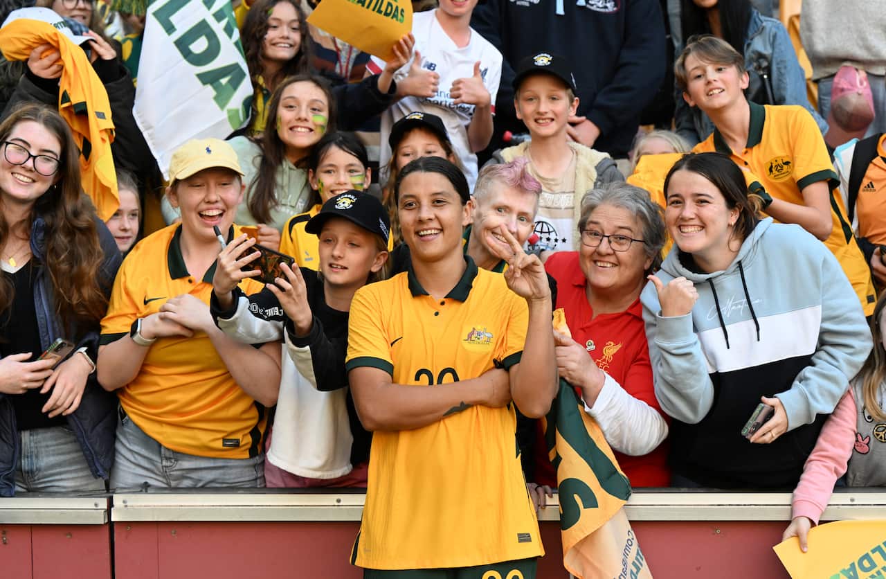 A woman in a yellow shirt holding up two fingers in a peace sign