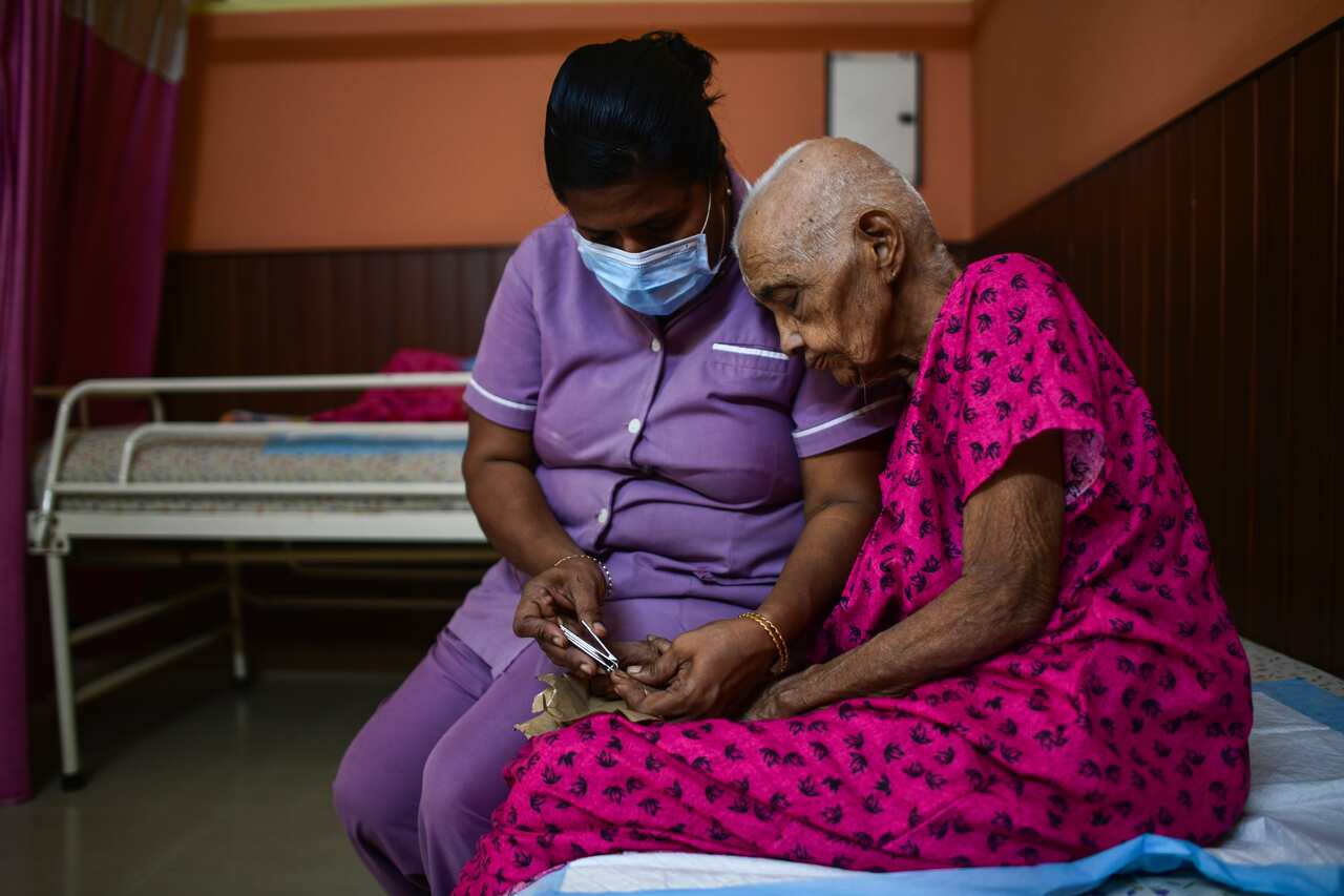 Mini, a nurse, trims the nails of an elderly woman