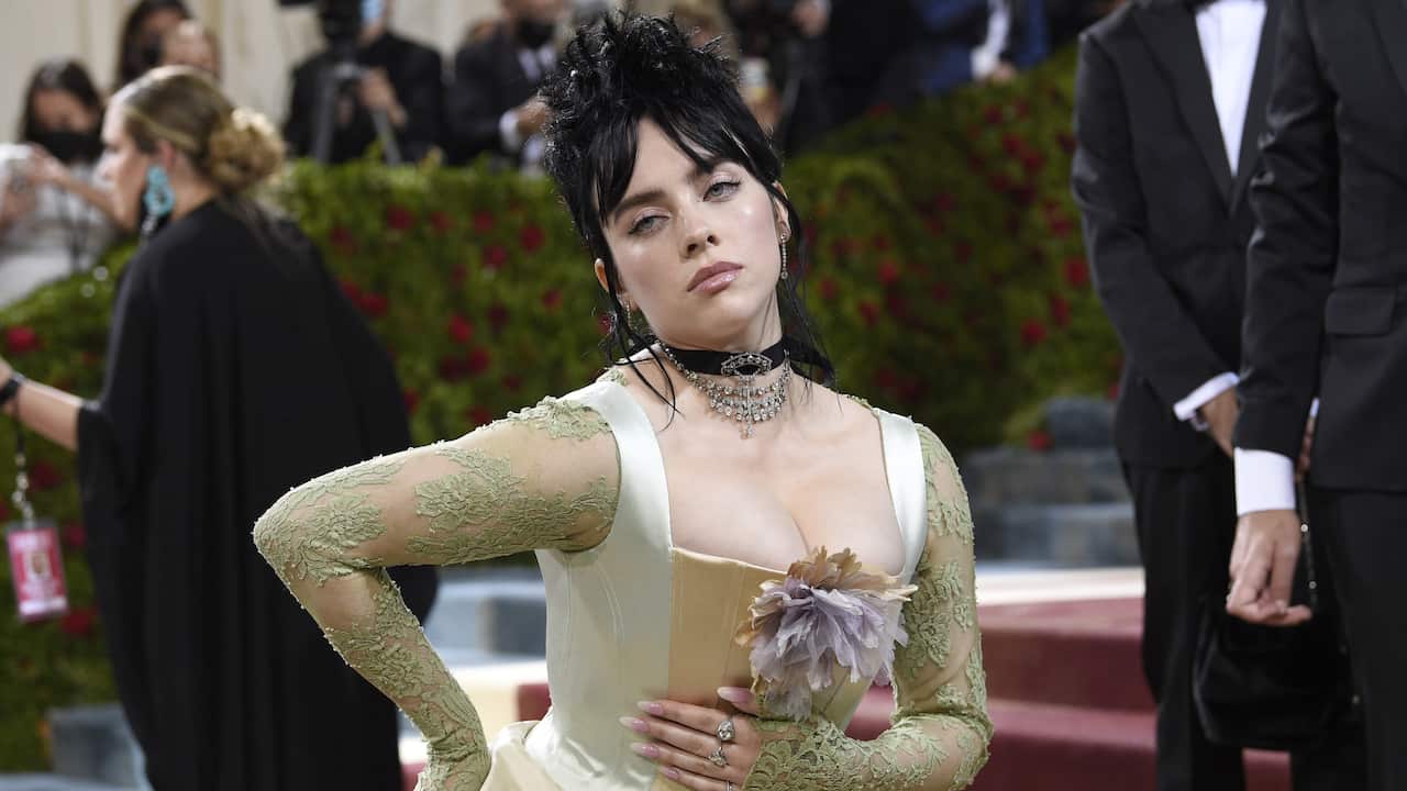 Billie Eilish wearing an ivory-coloured dress and posing for a photograph