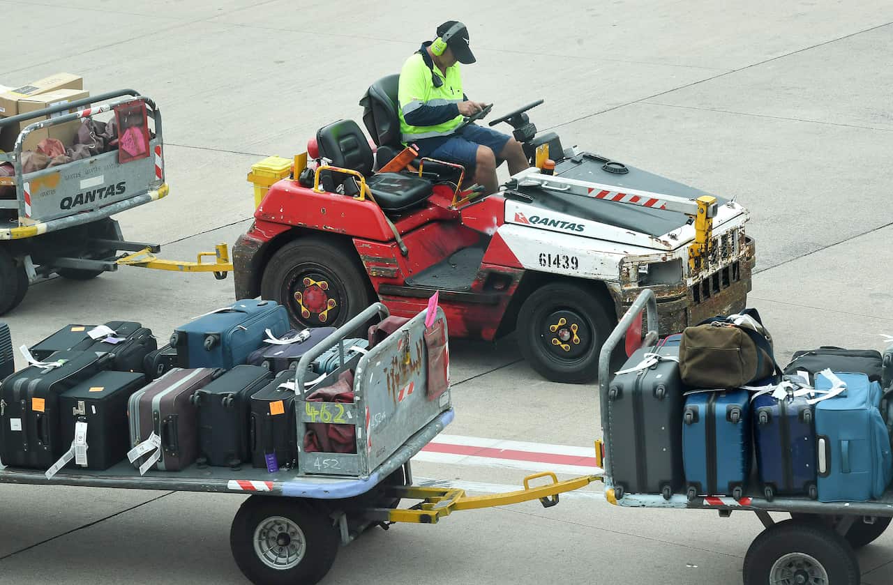 A luggage handler transporting suitcases on the airport tarmac