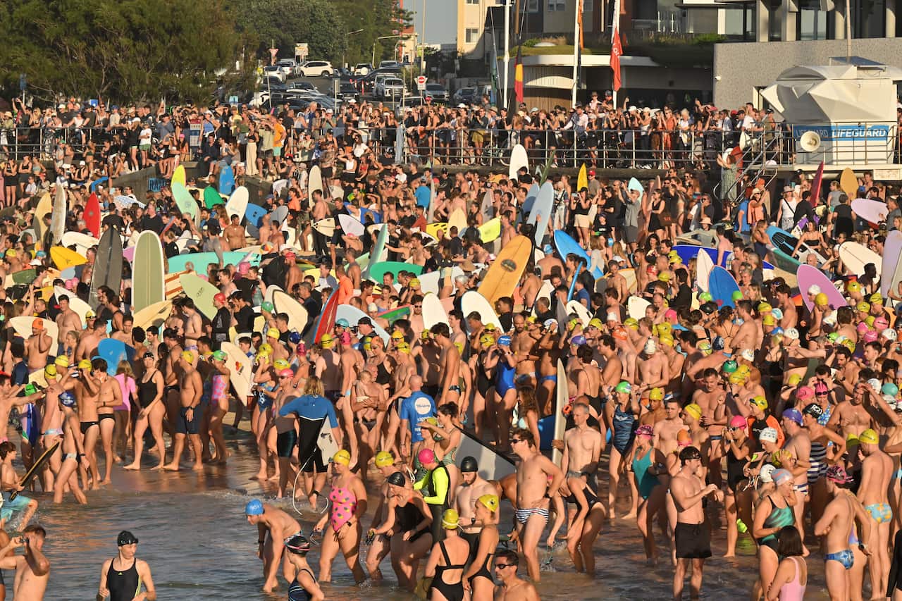 Large crowd gathered on the beach, many carrying boards.