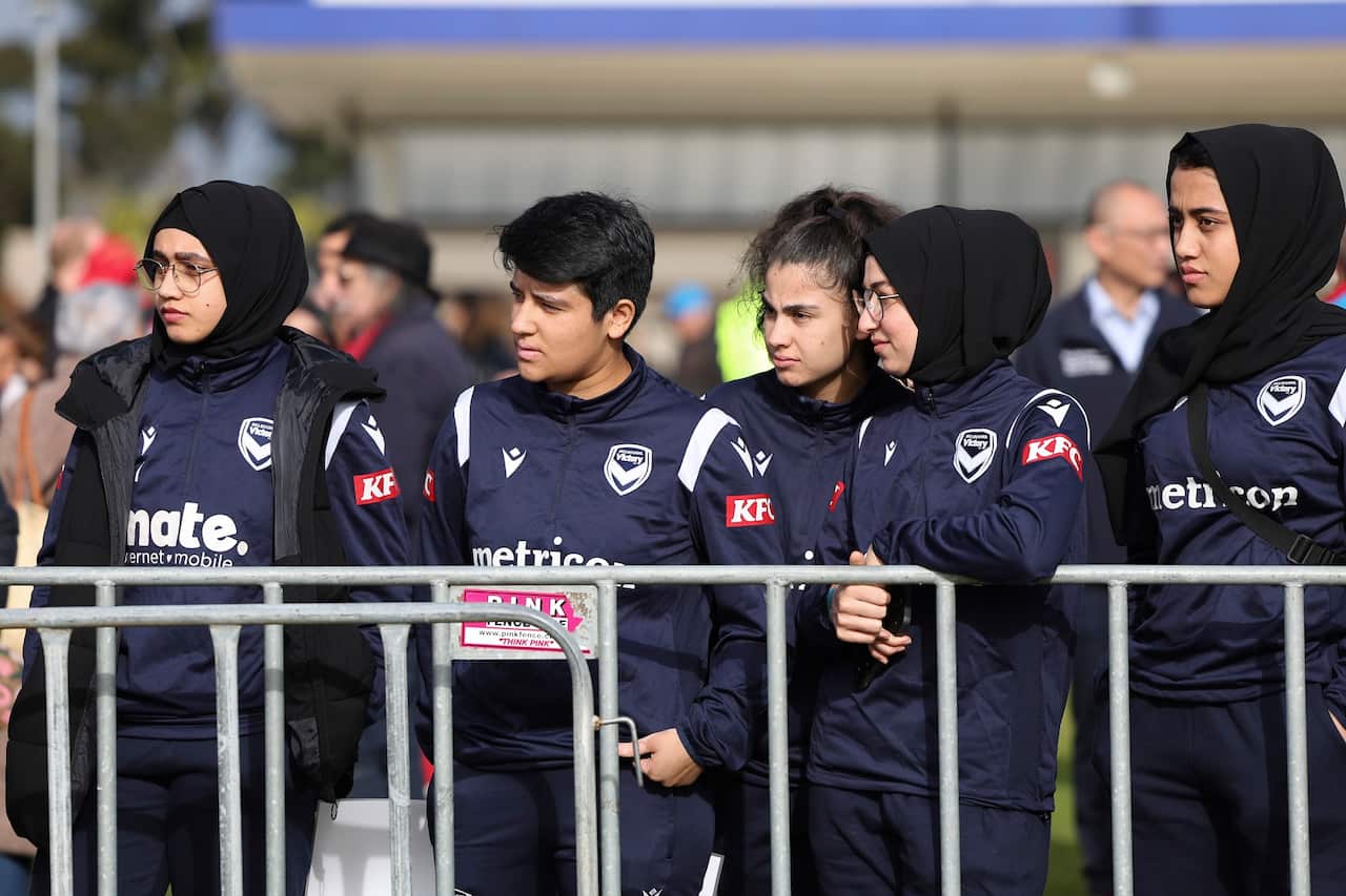 Five women in navy blue tracksuits. Four are wearing black hijabs.