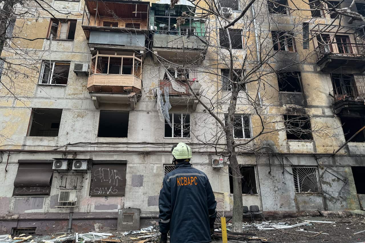 A man stands in front of a building that has been heavily damaged.