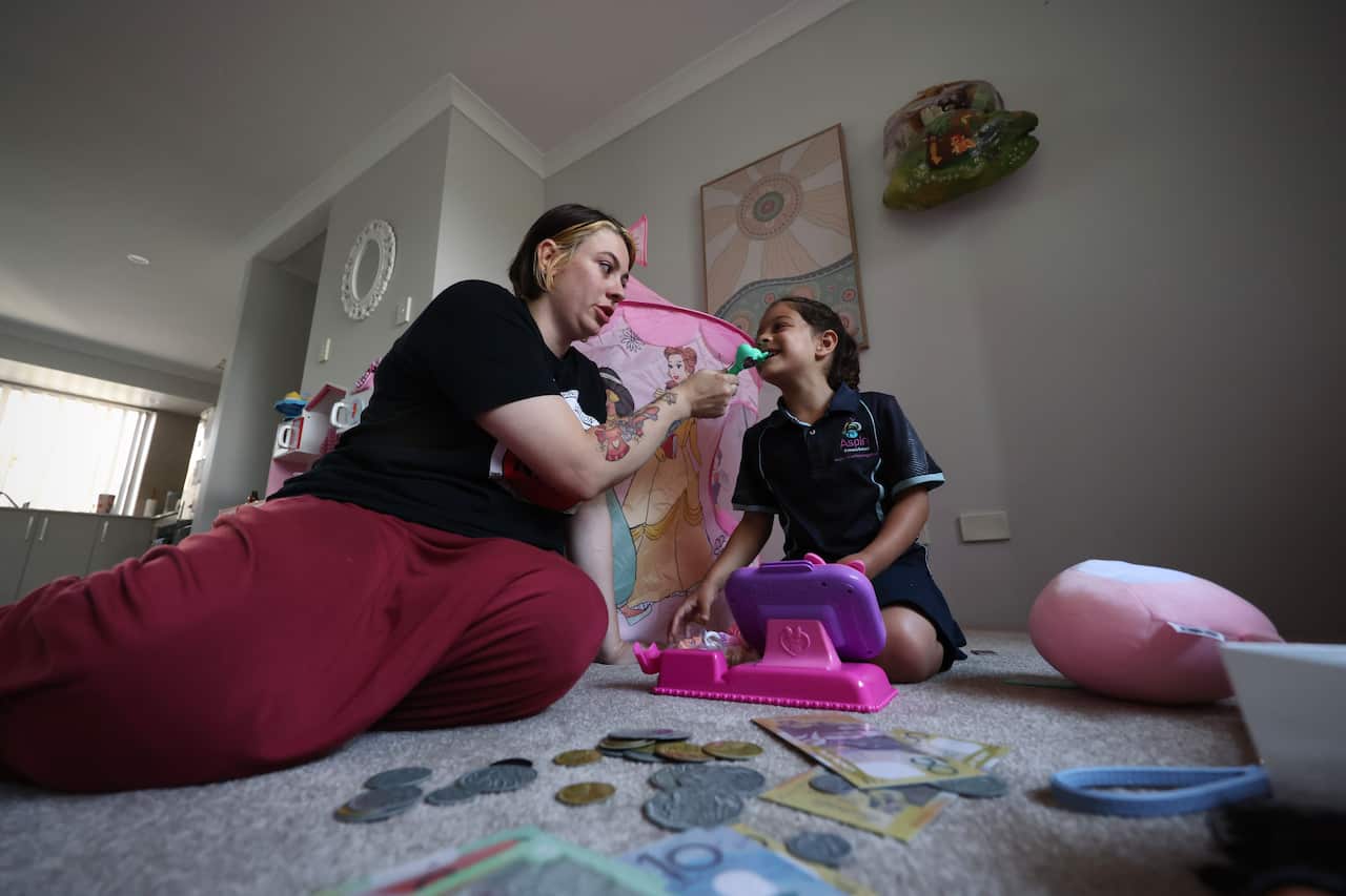 Mother and daughter sat down playing, with fake money notes on floor. 