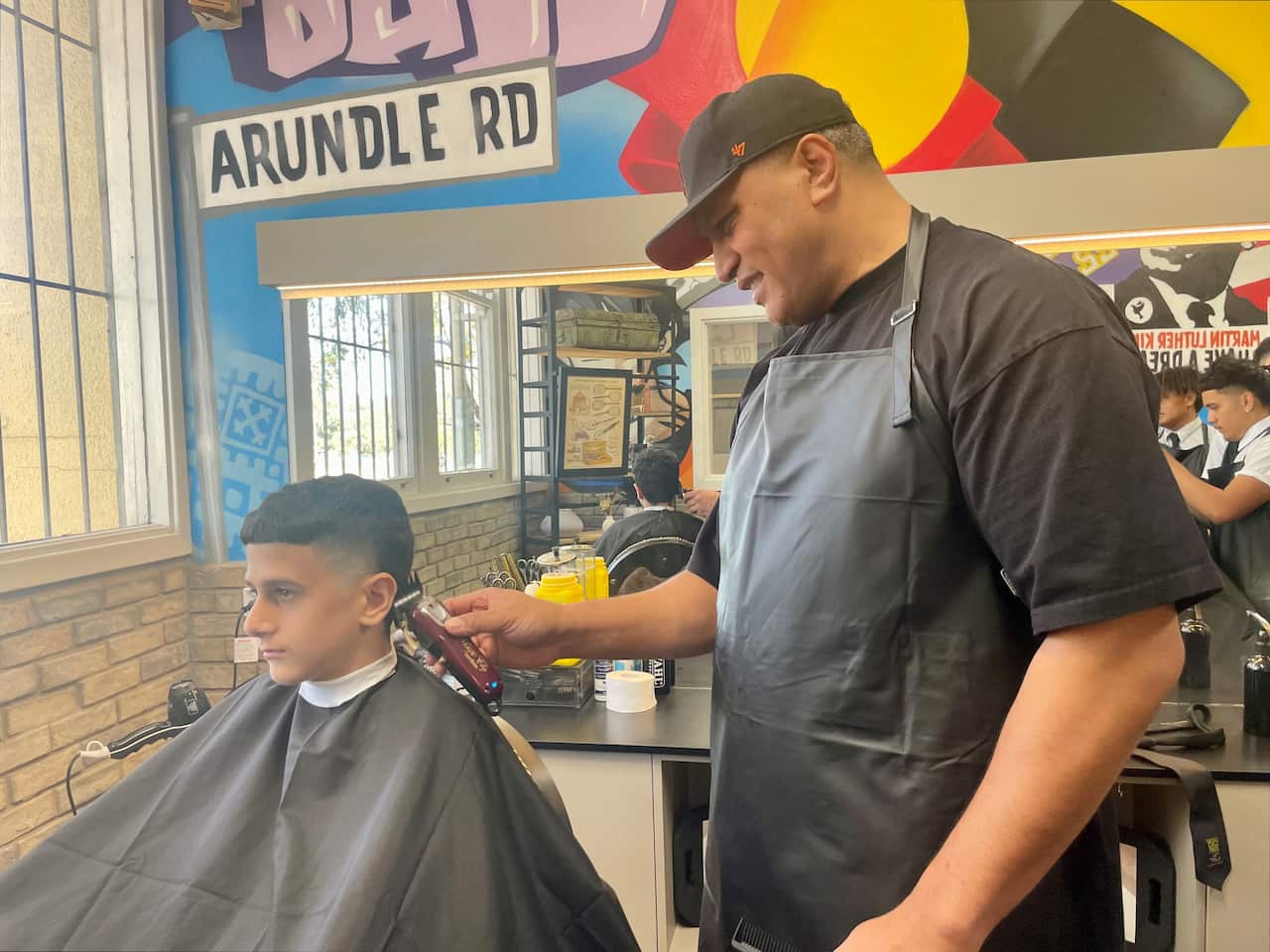 A barber smiles as he cuts a young boy's hair in a barber shop. 