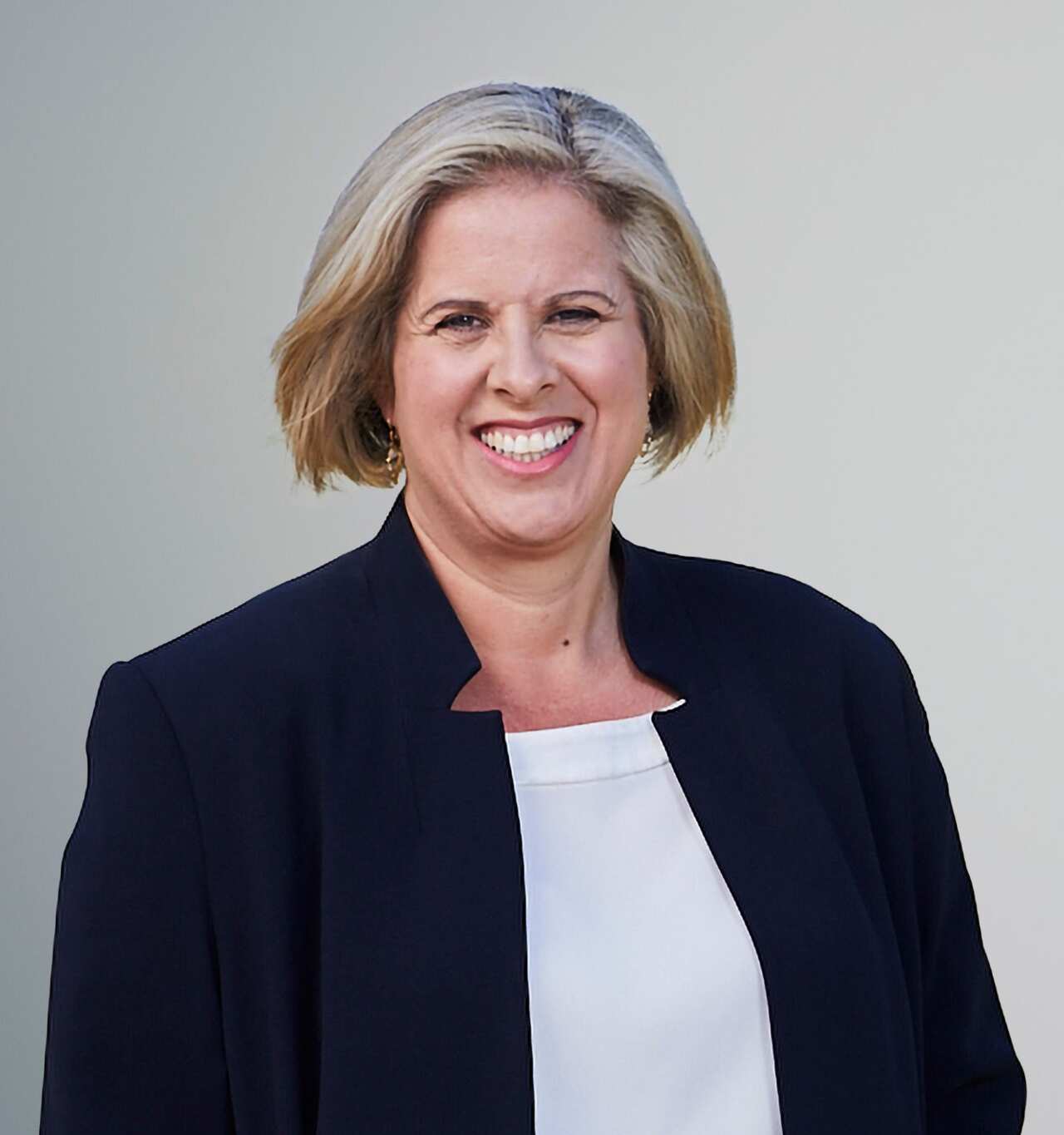 A woman in a navy jacket and white shirt smiles at the camera. 