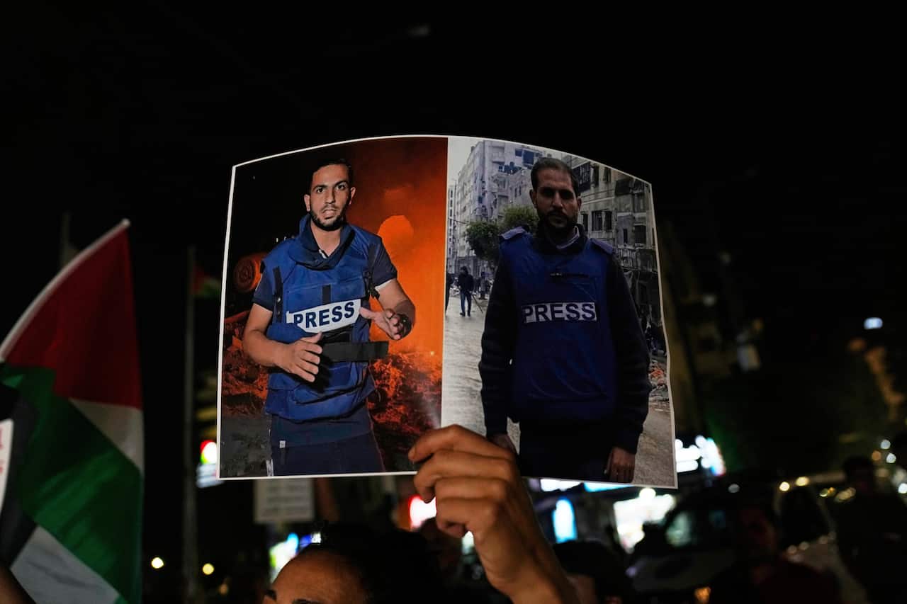 A hand holds up a poster of two killed journalists during a rally.