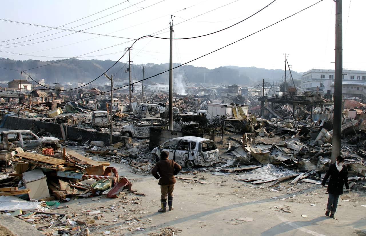 Two people walk among rubble and devastation caused by an earthquake and tsunami.