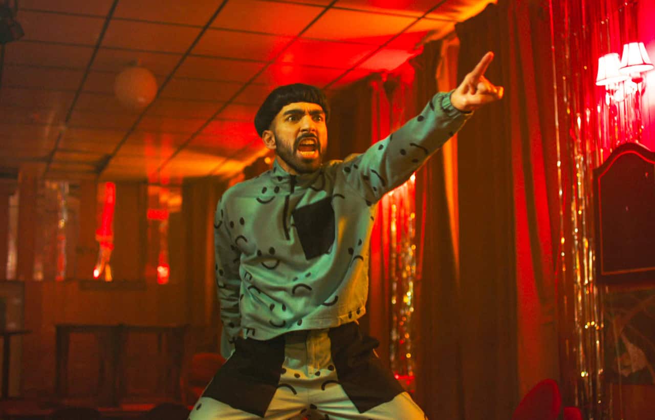 A man stands in a red-light room, with one hand pointing forward.