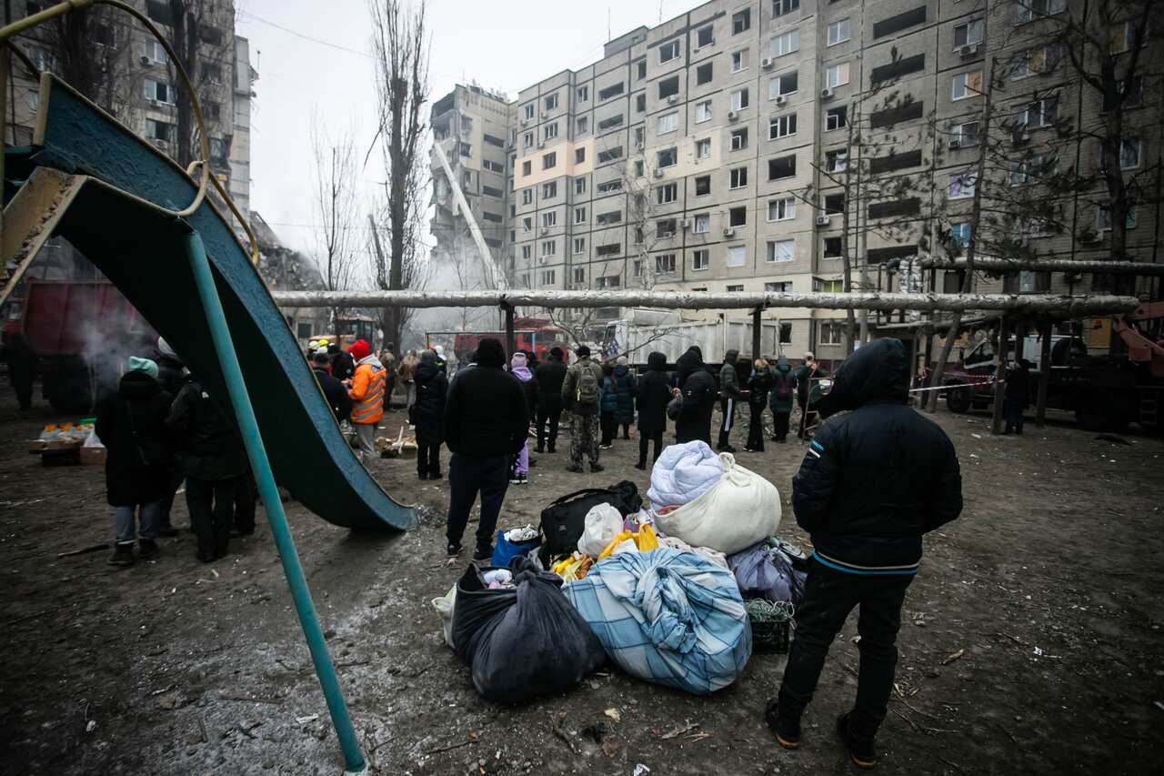 People standing in the cold looking at collapsed building