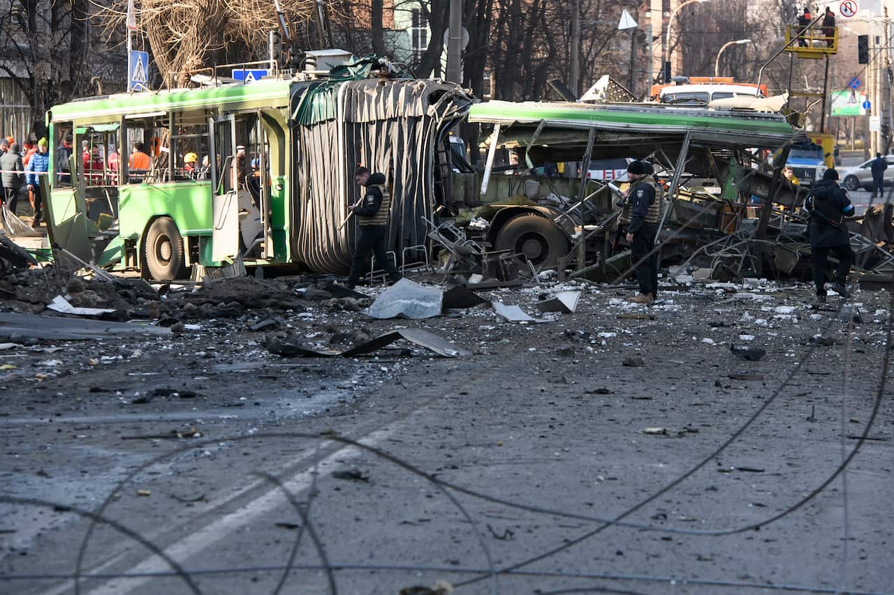 A destroyed trolleybus and car are seen on a street.