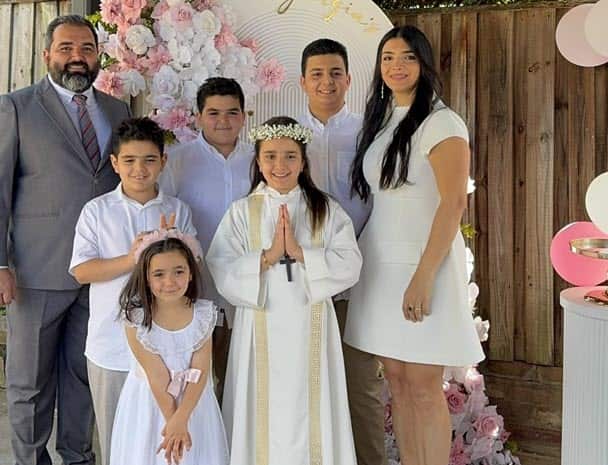 A family portrait featuring a couple and their five children posing in front of a white and pink floral backdrop.