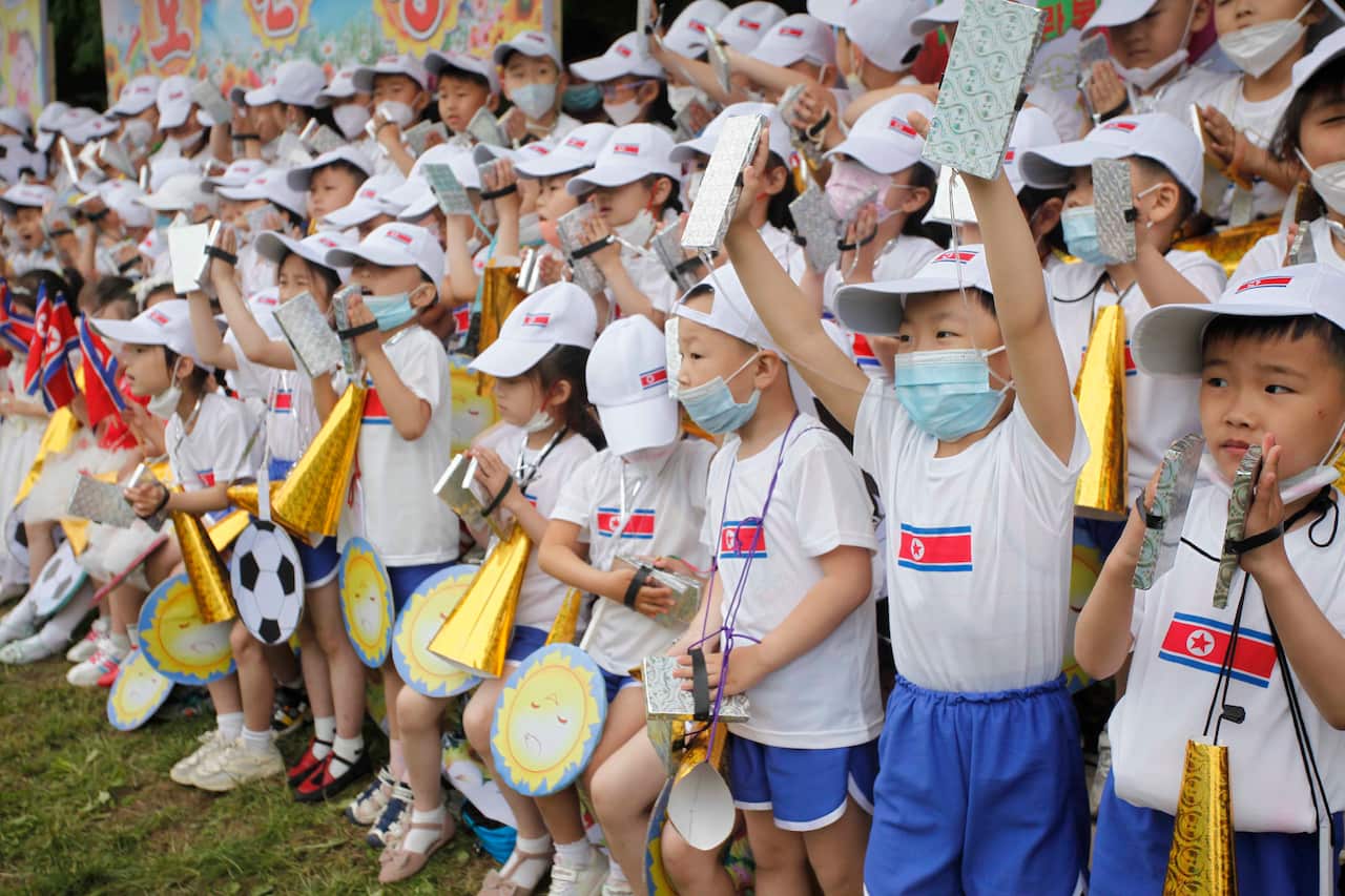 Children in white shirts and blue shorts. The shirt have the flag of North Korea on them.