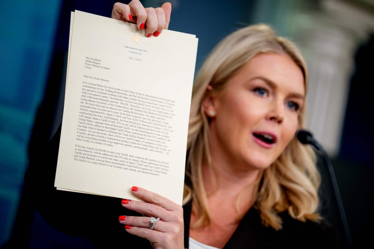 A woman with blonde hair holds up a document for the press to see.